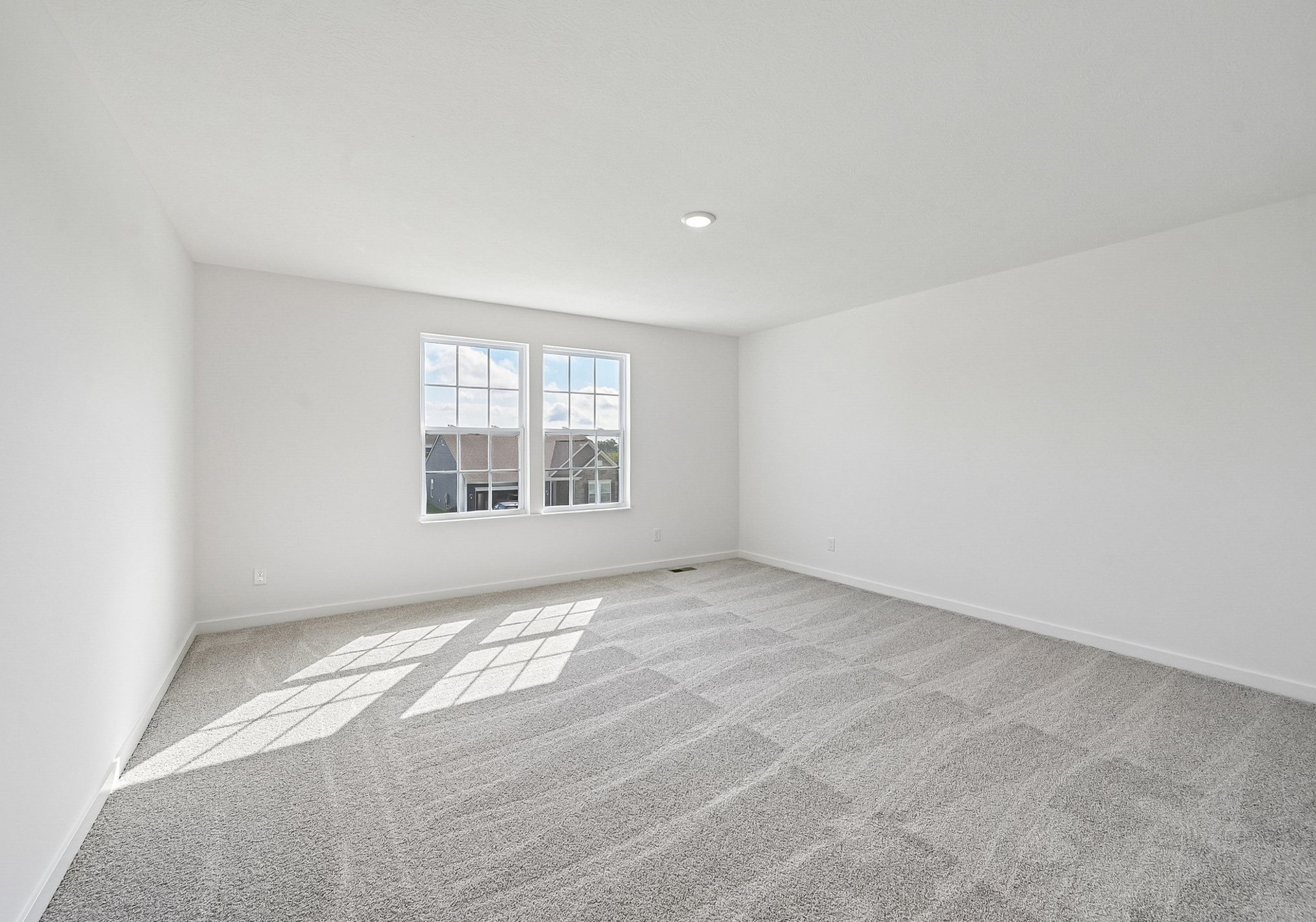 Empty room with beige carpeting and two large windows allowing natural light.