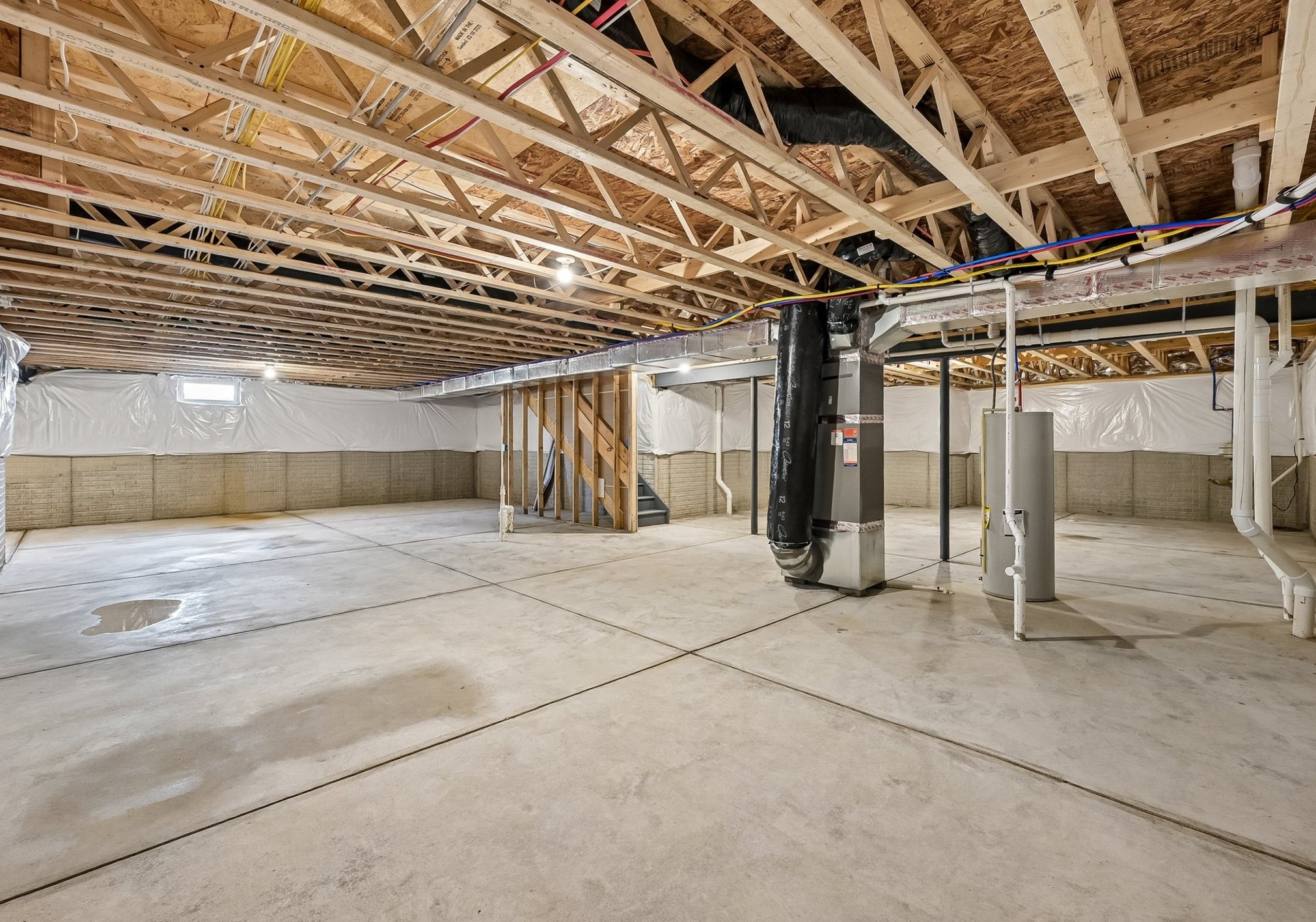 A spacious, unfinished basement with exposed wooden beams and concrete flooring.