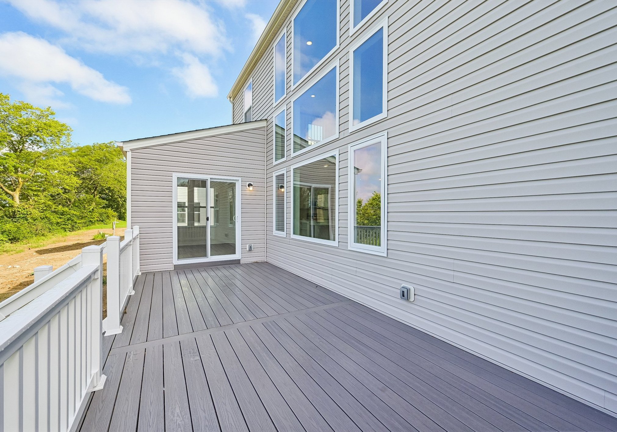 A sunny, spacious outdoor deck with light-colored composite flooring and large windows in the background.